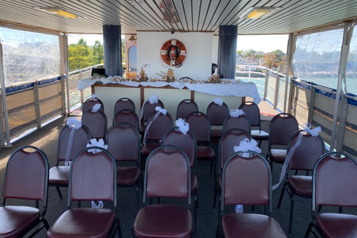 Deck set for an event, with rows of chairs decorated with white bows and a table at the front.
