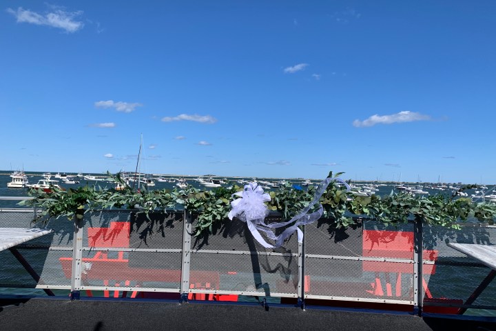 Decorated fence with greenery overlooking a marina with boats under a clear blue sky.