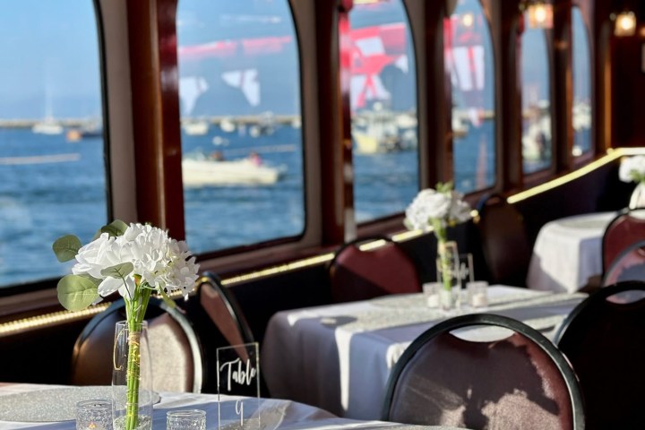 Elegant dining area on a boat with ocean view, set tables, and flowers.