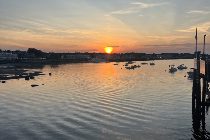 Sunset over a calm harbor with boats and a rippling water surface.