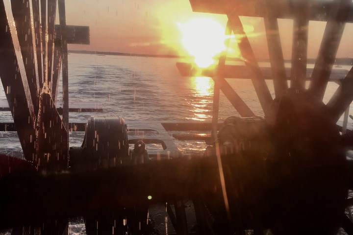 Sunset over water with silhouettes of water wheel paddles in foreground.