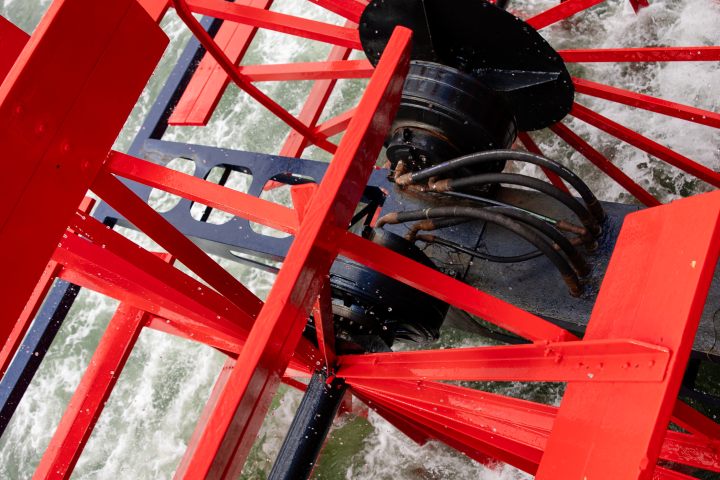Close-up of a red paddle wheel turning in water.