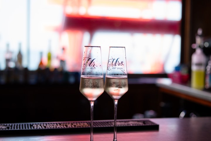 Two champagne glasses on a bar labeled 'Mr. and Mrs. EST 2025' with blurred background.