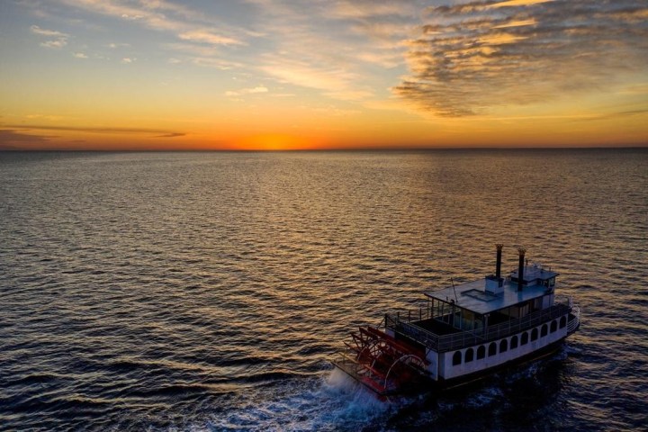 Steamboat on ocean at sunset with orange sky and clouds.